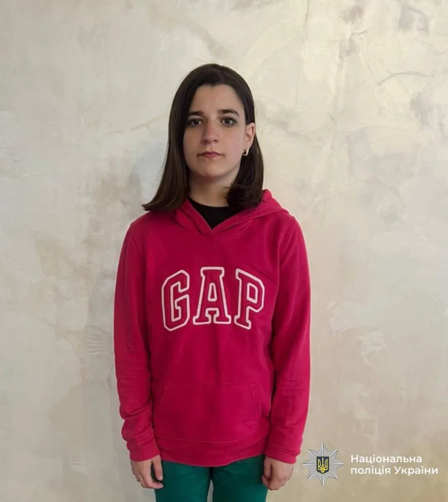 Дитина у червоній худі GAP стоїть біля стіни