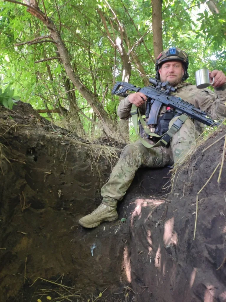 Військовий відпочиває в окопі з гвинтівкою і кухлем