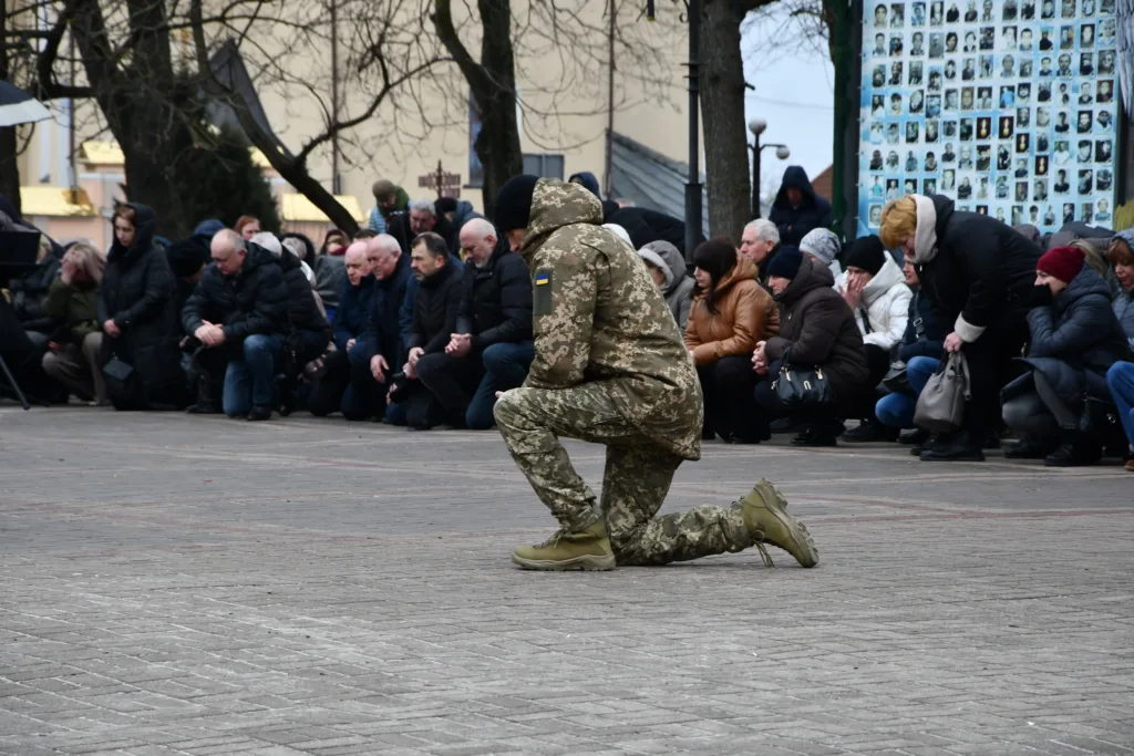 Військовий і люди на колінах під час вшанування