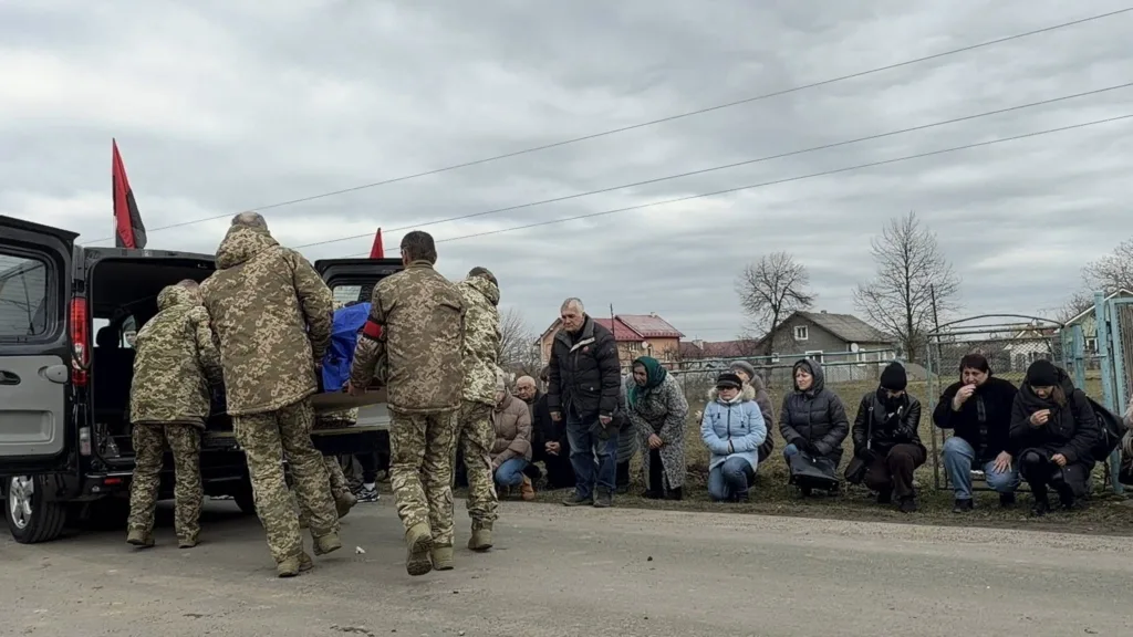 Військові несуть труну, люди стоять на колінах