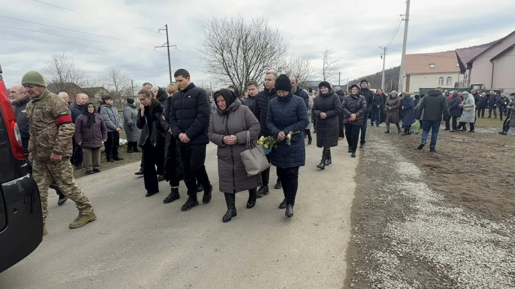 Люди йдуть дорогою під час похоронної процесії
