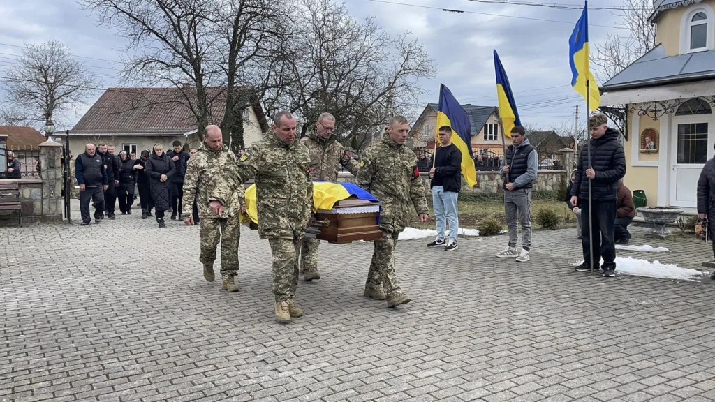 Військові несуть труну, накриту українським прапором