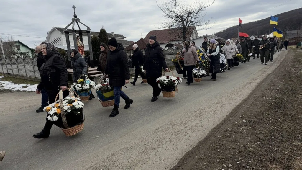 Похоронна процесія з квітами та прапорами в селі