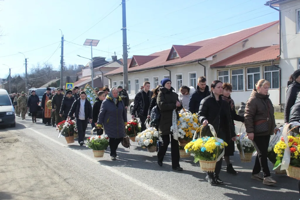 Люди несуть квіти на похоронній процесії вулицею