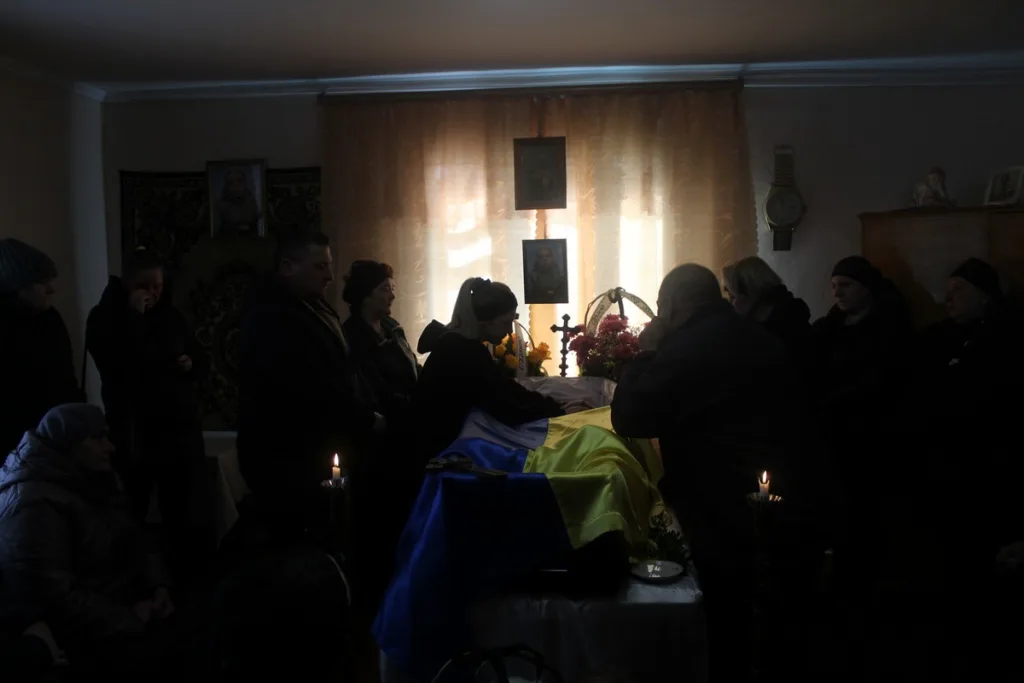 Люди прощаються з полеглим, накритим українським прапором.