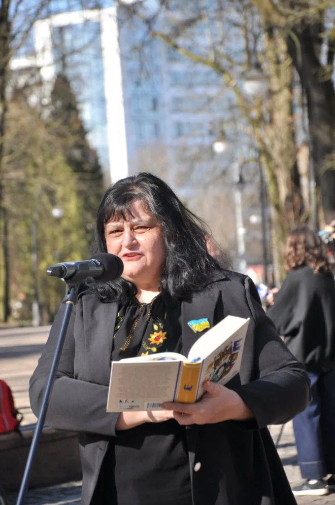 Жінка читає книгу біля мікрофона на вулиці