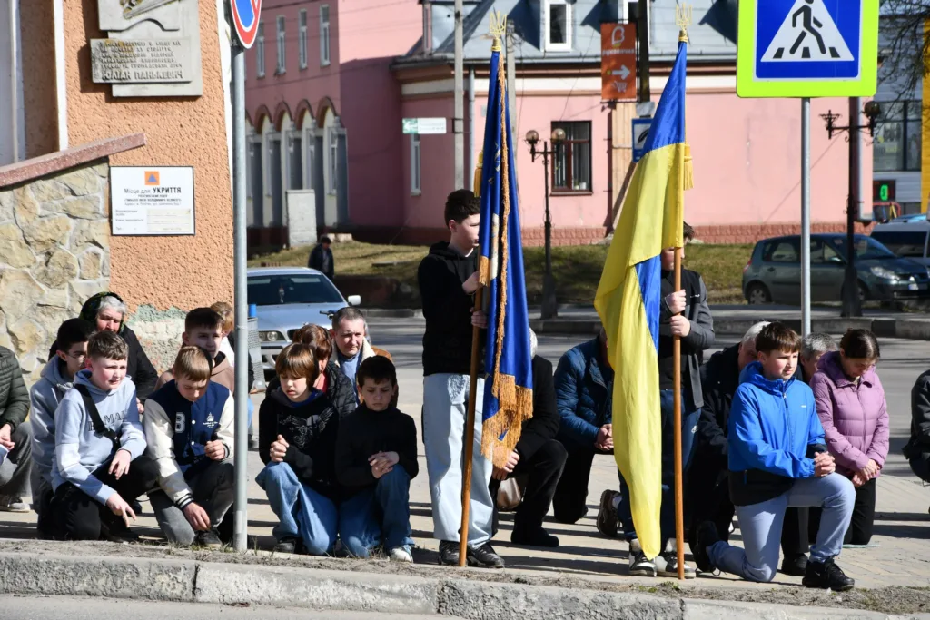 Діти з прапорами України стоять на колінах