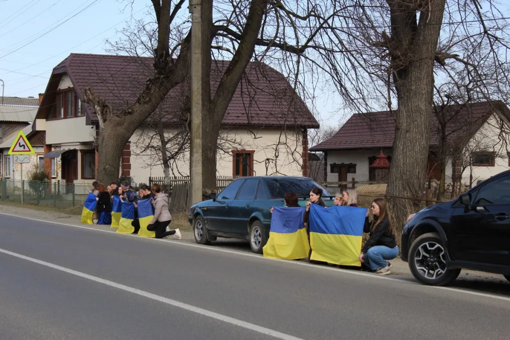 Люди з прапорами України стоять обабіч дороги