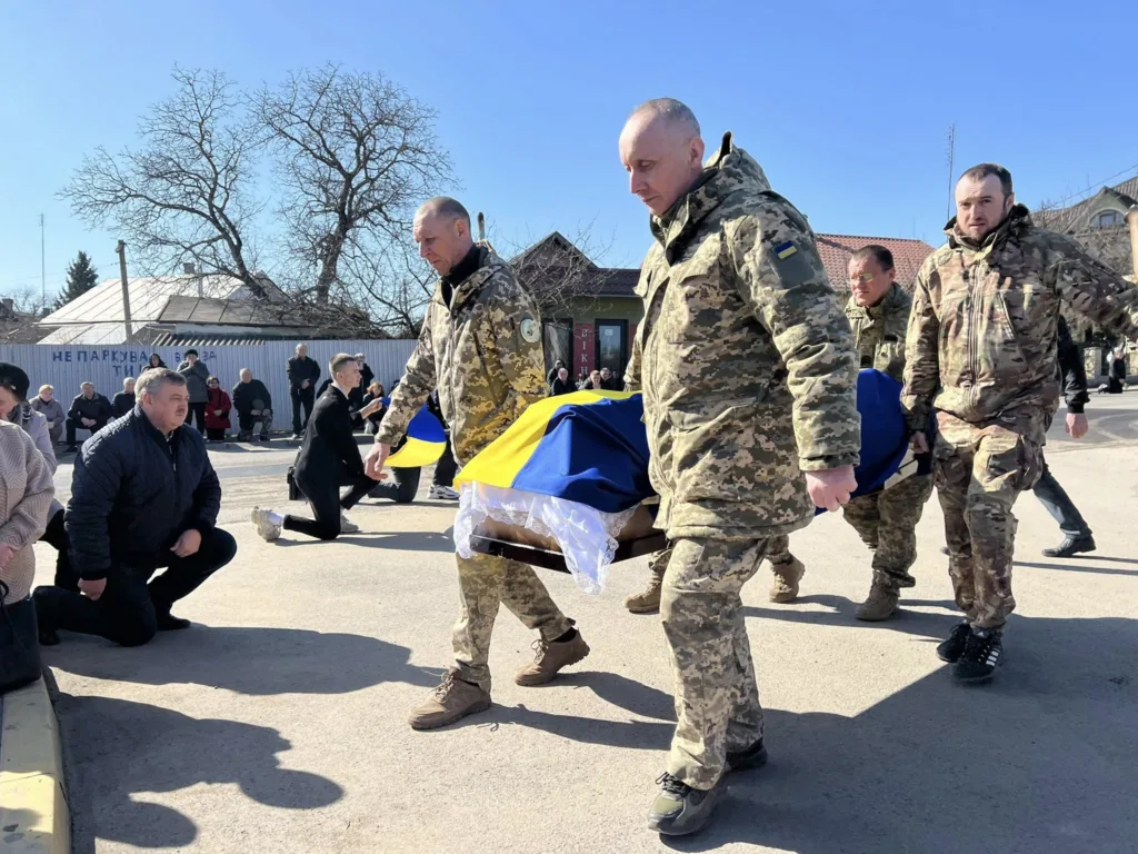 Військові несуть труну, накриту українським прапором