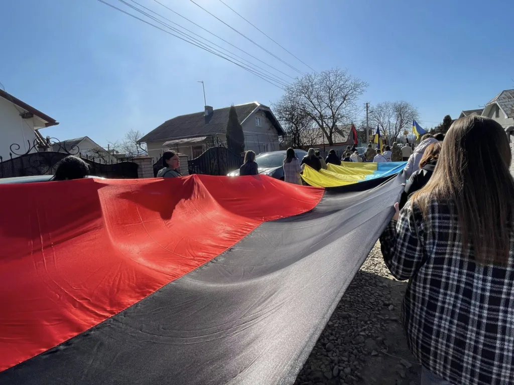 Люди несуть великий червоно-чорний прапор на вулиці