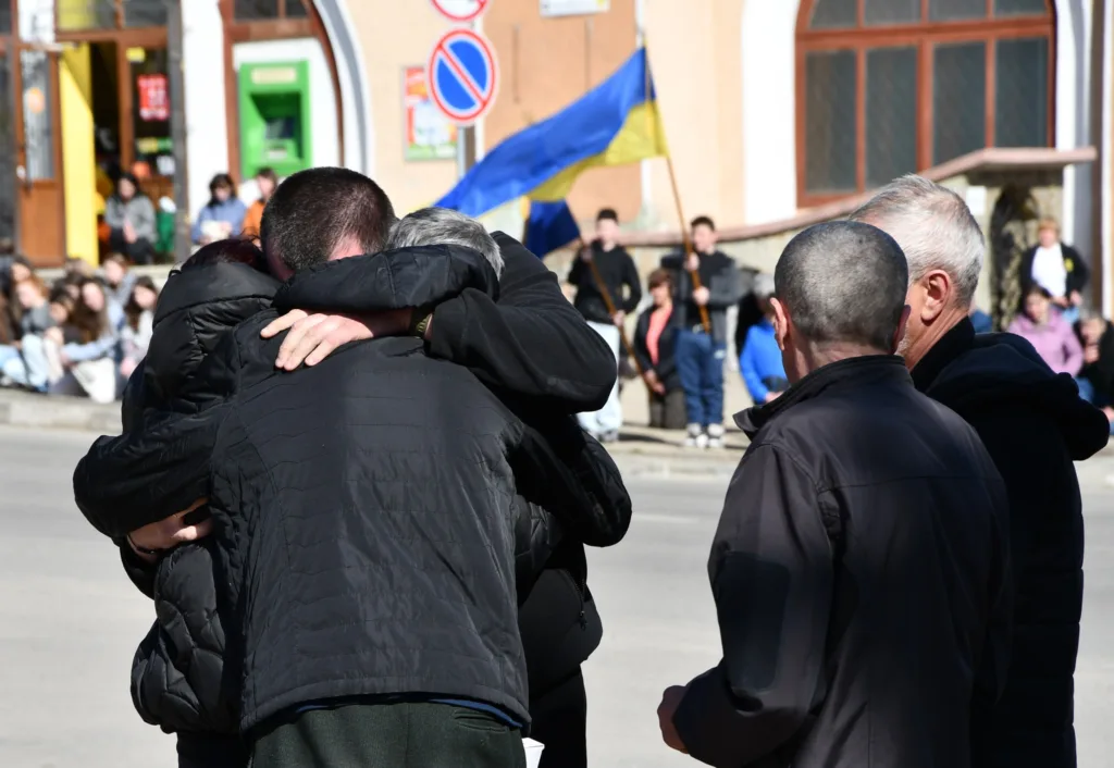 Люди обіймаються на вулиці біля прапора України