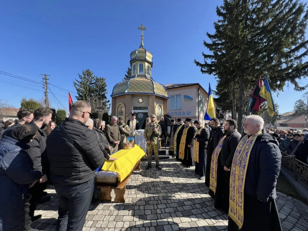 Похорон воїна біля церкви з українськими прапорами