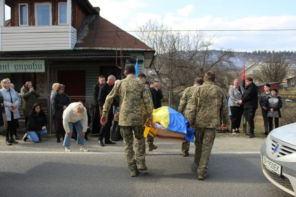 Військові несуть труну, накриту українським прапором