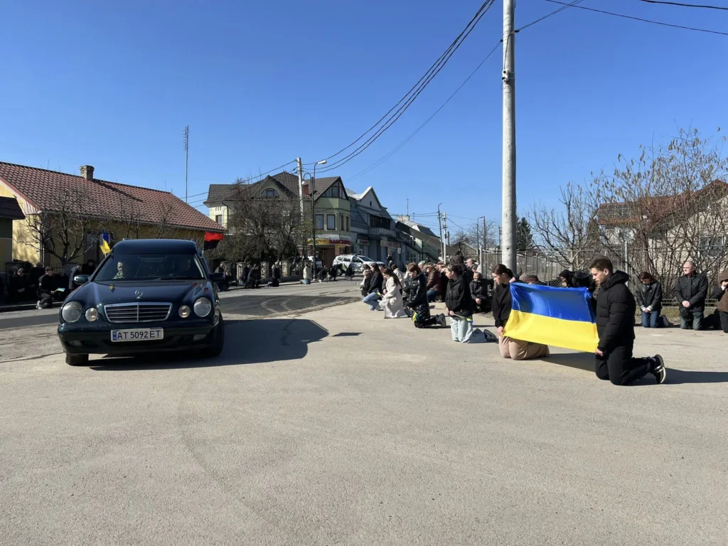 Люди на колінах з українським прапором на вулиці