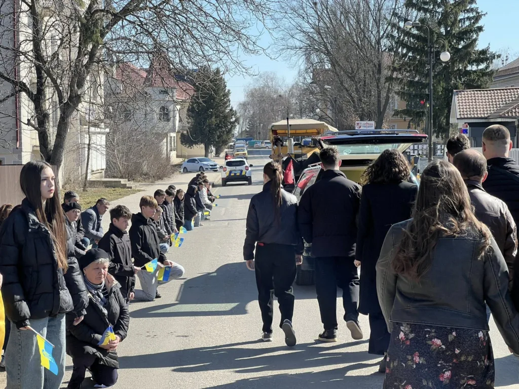 Люди з українськими прапорами стоять на колінах на вулиці