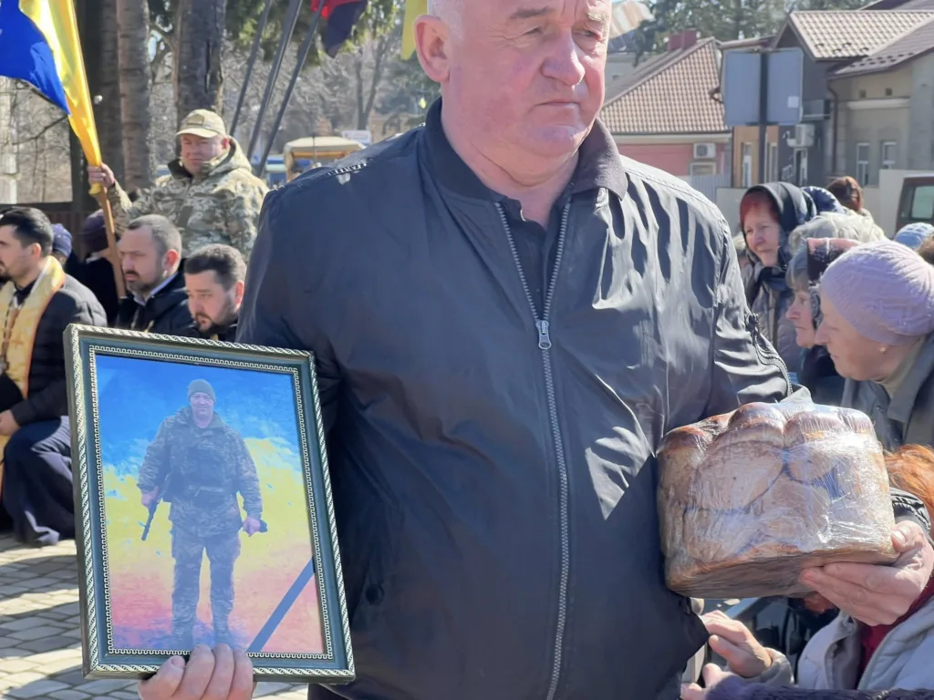 Чоловік тримає портрет військового та хліб на церемонії