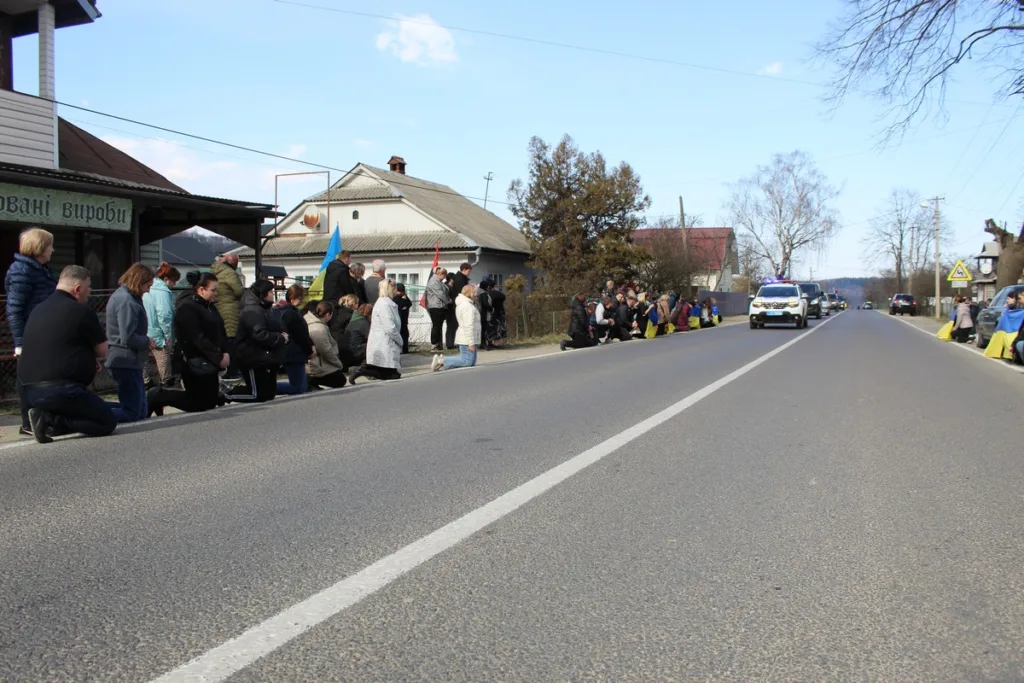 Люди на колінах уздовж дороги з прапорами України