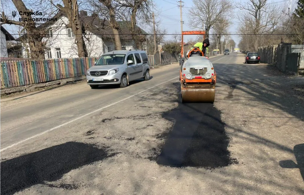 Робітник ремонтує асфальт дороги дорожнім катком
