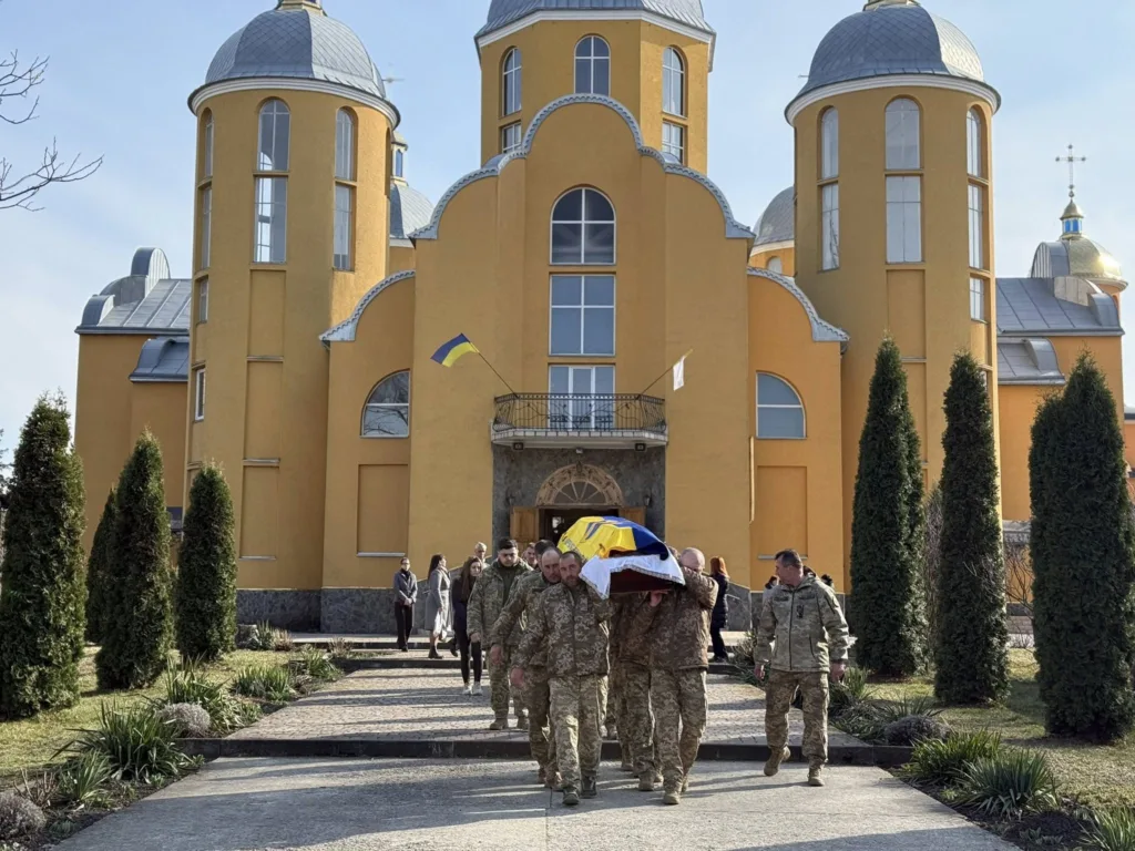 Військові несуть труну з прапором України біля церкви