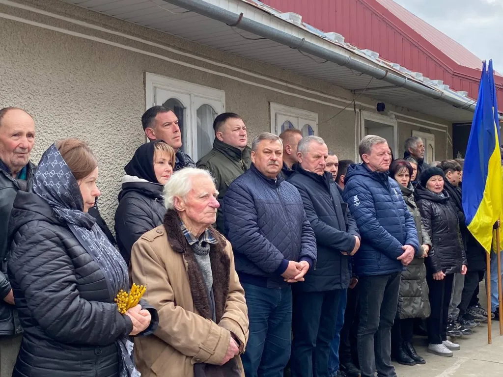 Люди стоять під українським прапором біля будівлі