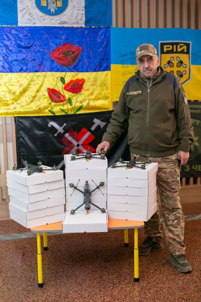 Військовий передає дрони на тлі українських прапорів