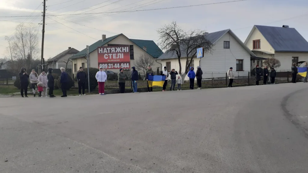 Люди стоять з українськими прапорами біля будинків