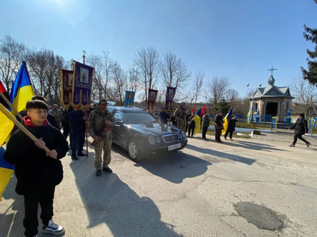 Похоронна процесія біля каплиці з українськими прапорами