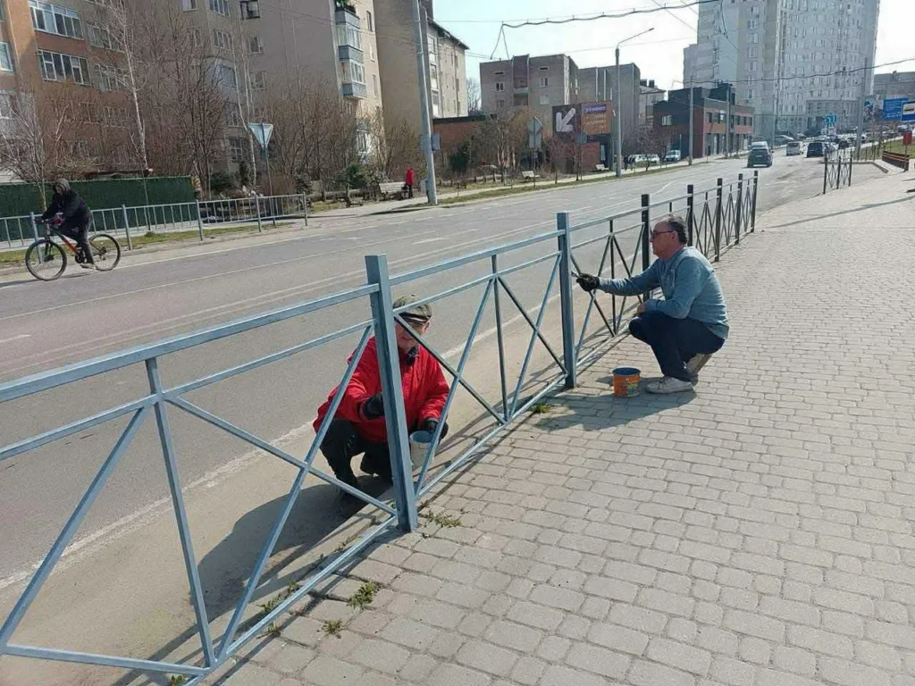 Люди фарбують металеву огорожу біля дороги