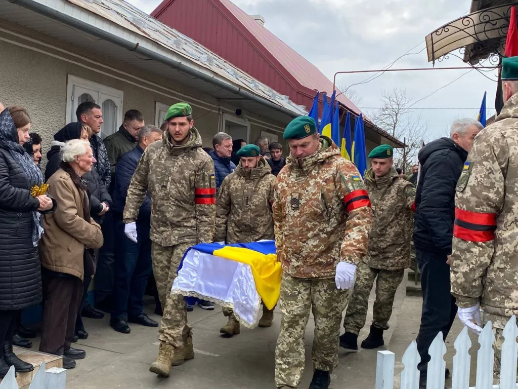 Військові несуть труну, накриту українським прапором