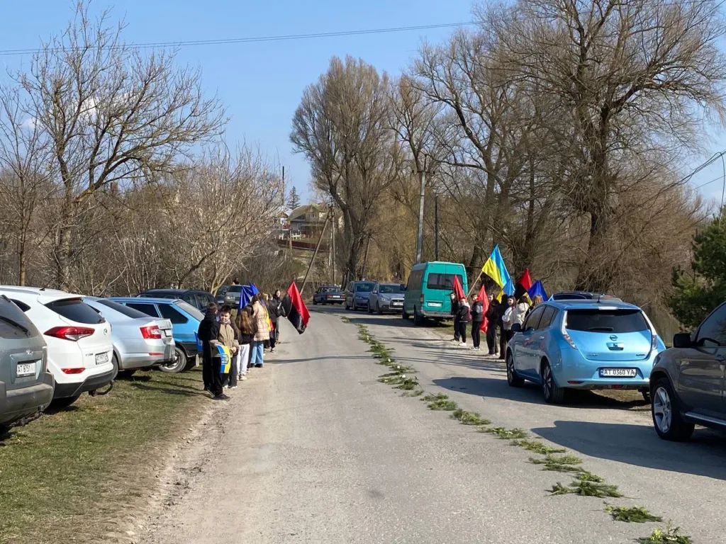 Люди з українськими прапорами стоять уздовж дороги