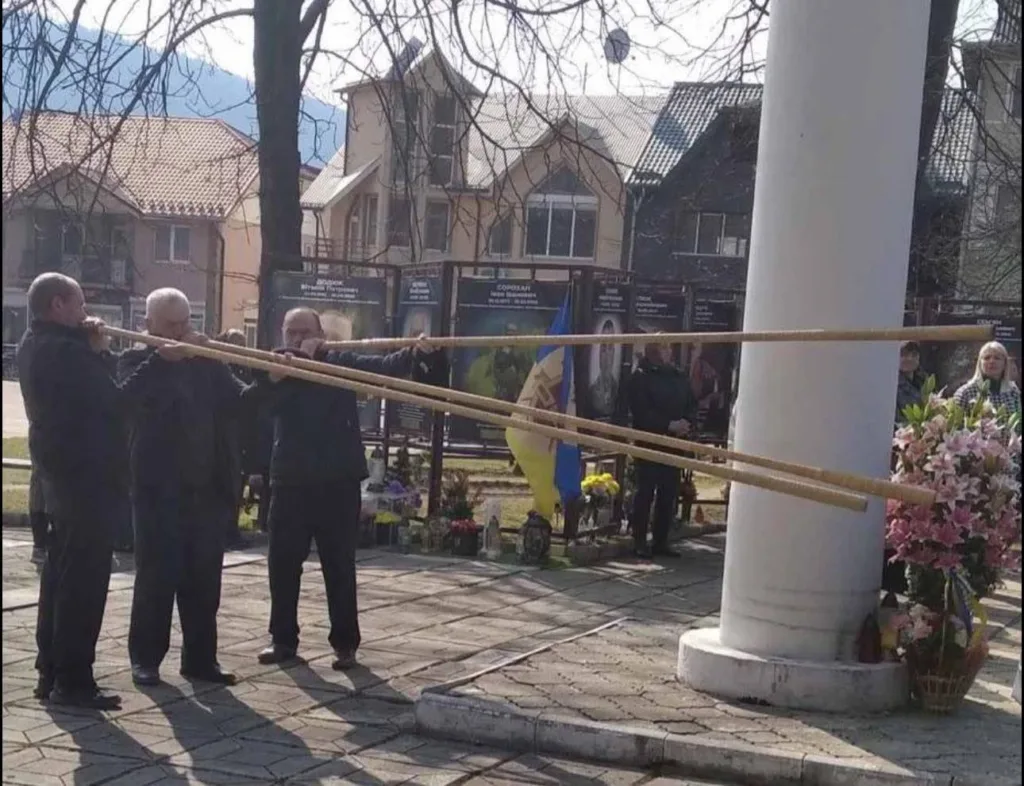 Чоловіки грають на трембітах біля пам’ятника