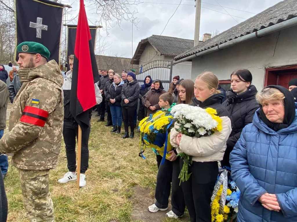 Люди на похороні воїна з квітами та прапорами