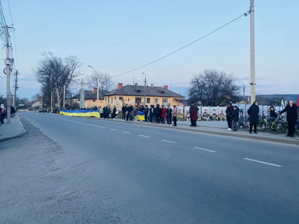 Люди стоять біля дороги з українським прапором