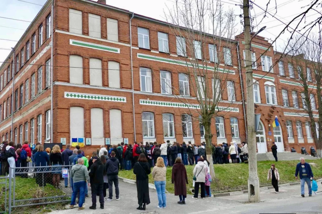 Черга людей біля червоної цегляної будівлі школи