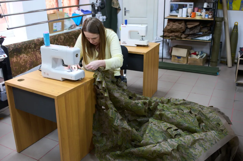 Жінка шиє камуфляжну сітку на швейній машині