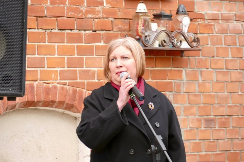 Жінка говорить у мікрофон біля цегляної стіни