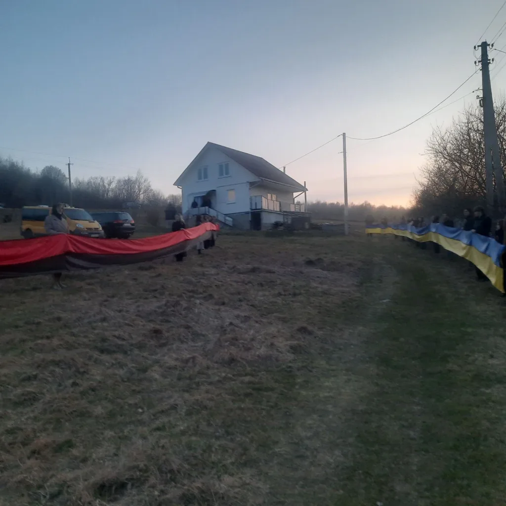 Люди тримають український і червоно-чорний прапори біля будинку