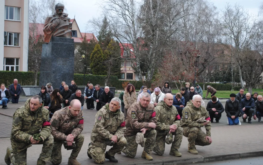 Військові та люди стоять на колінах біля пам’ятника