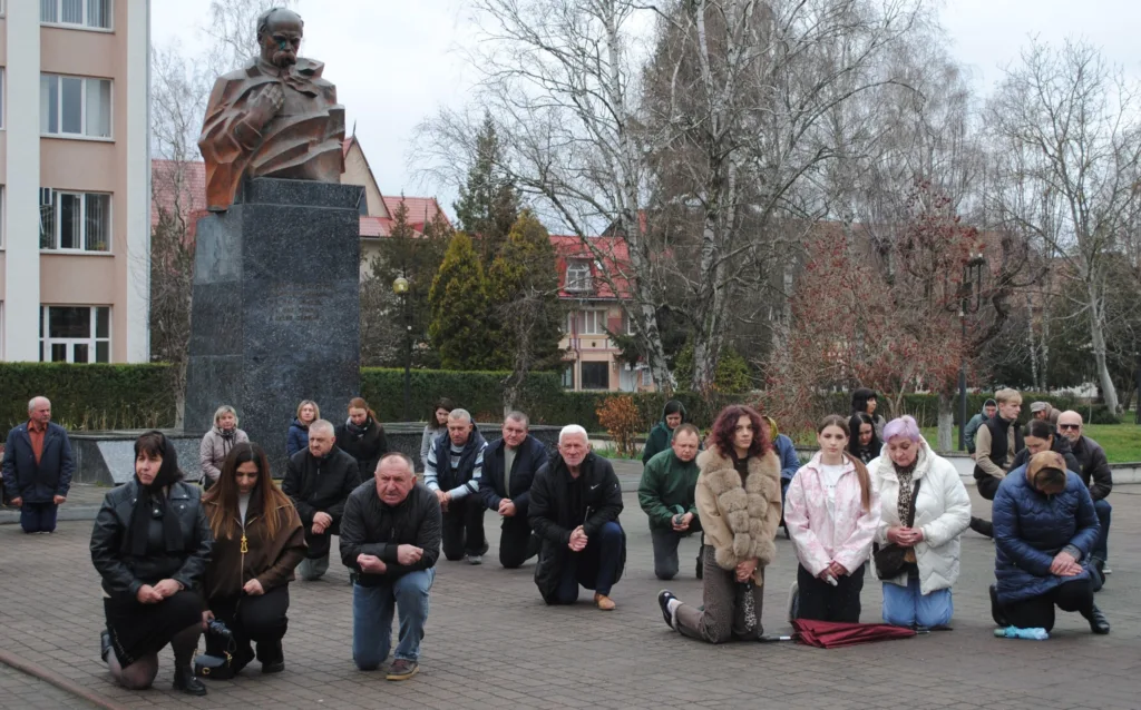 Люди на колінах біля пам'ятника у парку