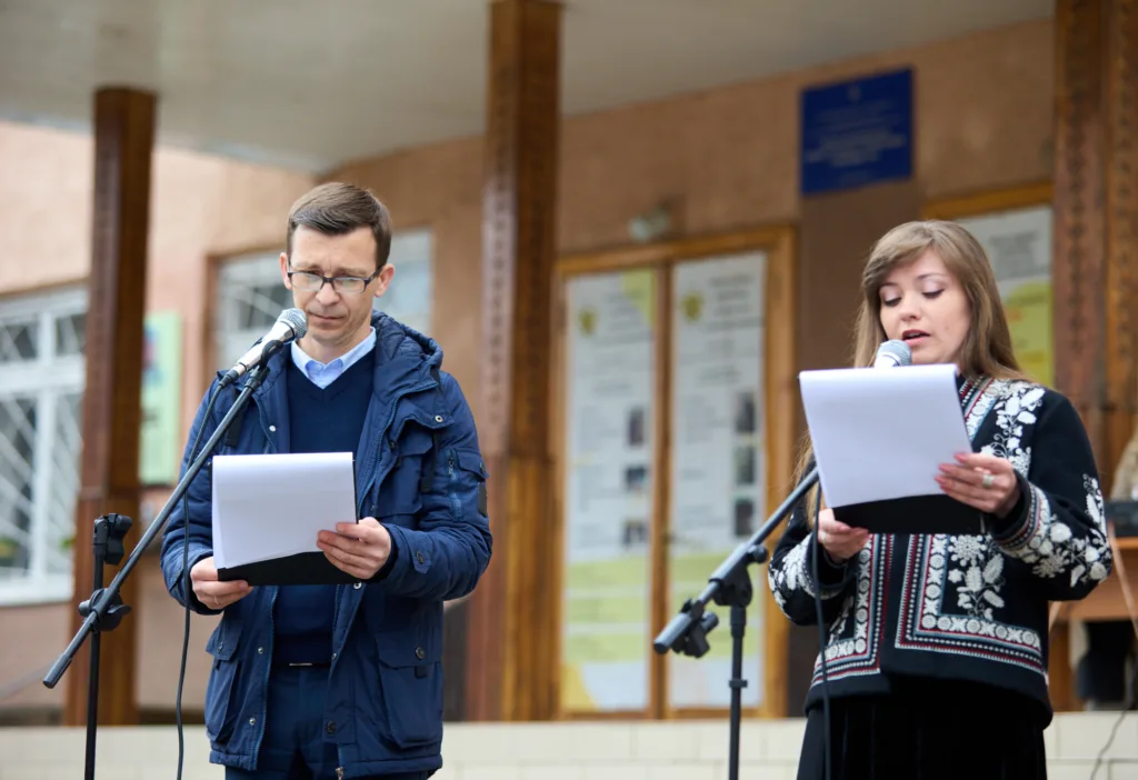Двоє людей читають тексти на мікрофонах надворі