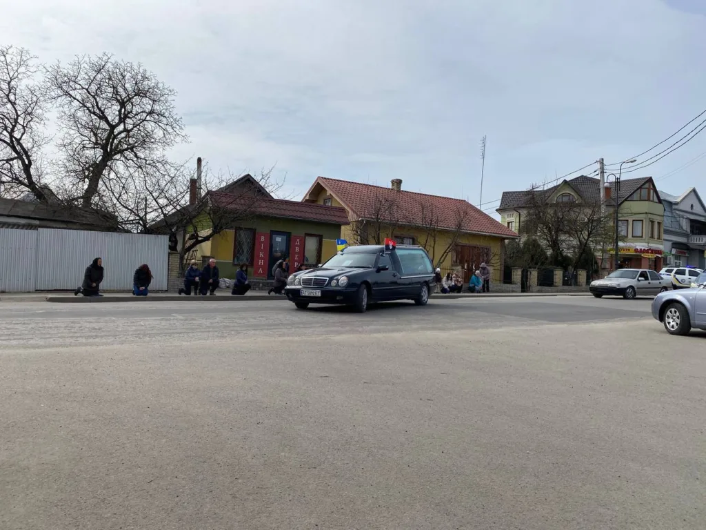 Люди на колінах біля дороги під час процесії