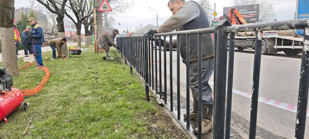 Робітники фарбують паркан біля дороги