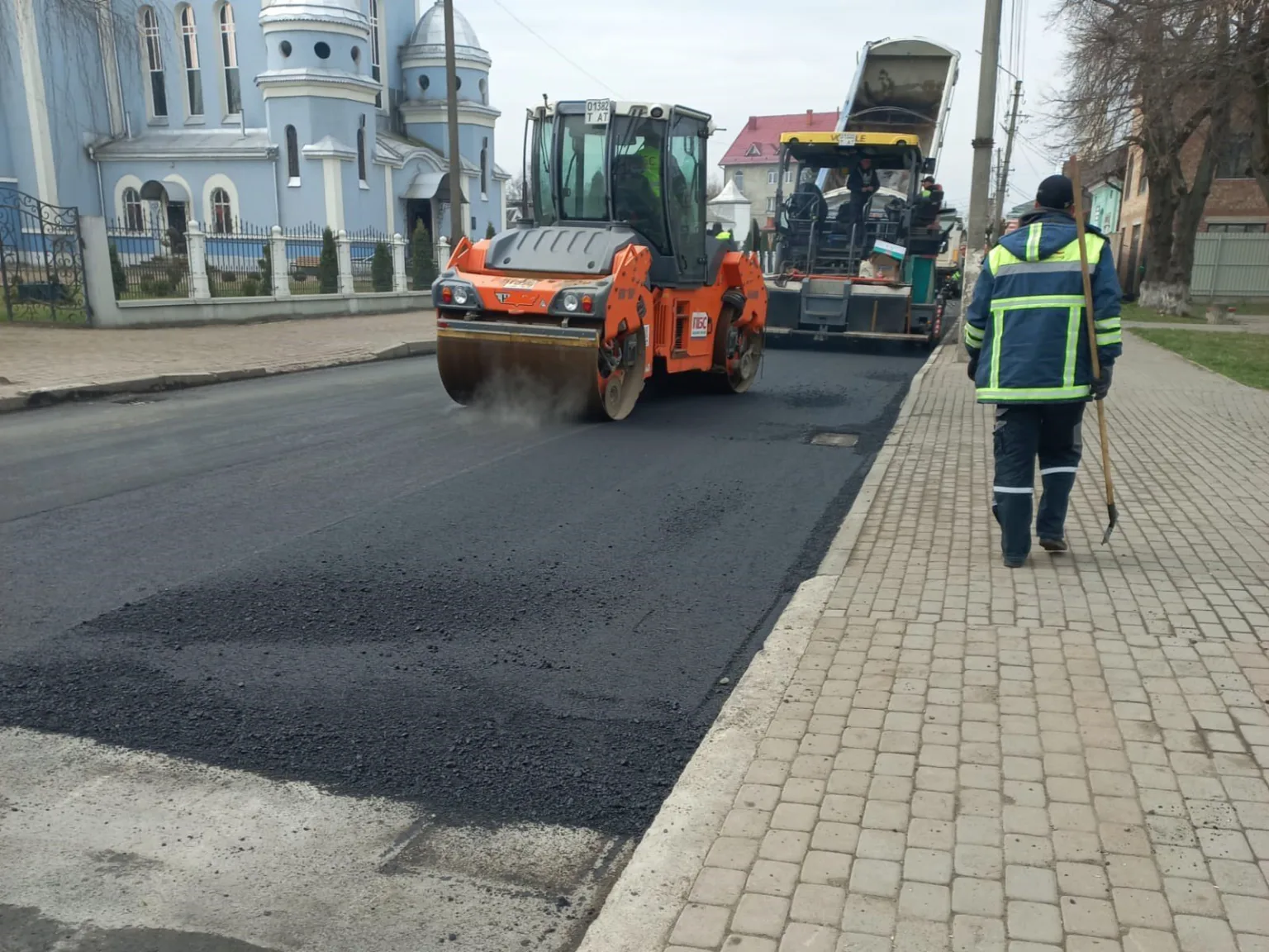 Робітники ремонтують дорогу асфальтоукладачем біля церкви