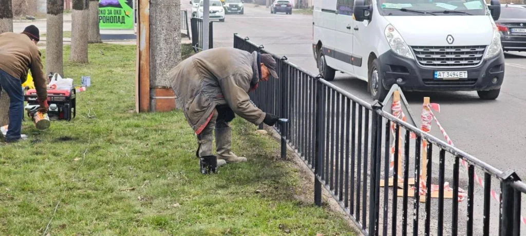 Робітники фарбують паркан біля дороги