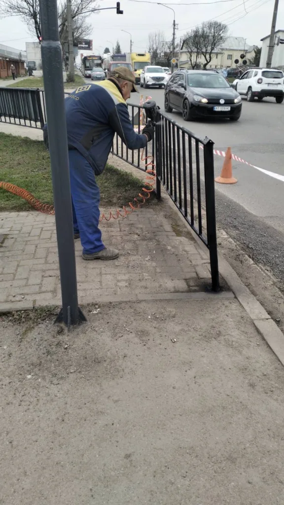 Робітник фарбує металеву огорожу біля дороги
