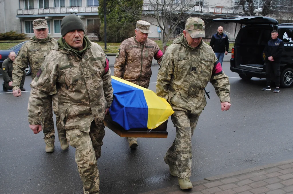 Військові несуть труну, вкриту українським прапором