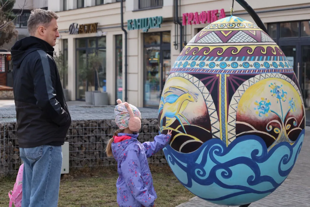 Дитина розглядає велику розписану писанку на вулиці