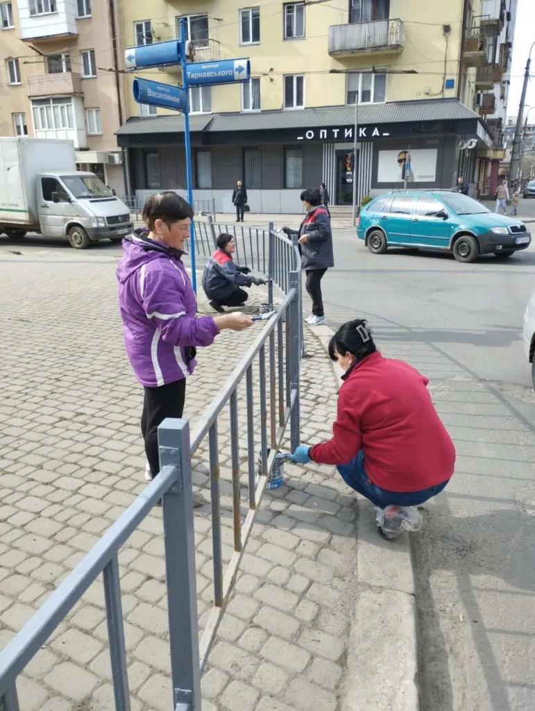 Люди фарбують паркан біля дороги у місті