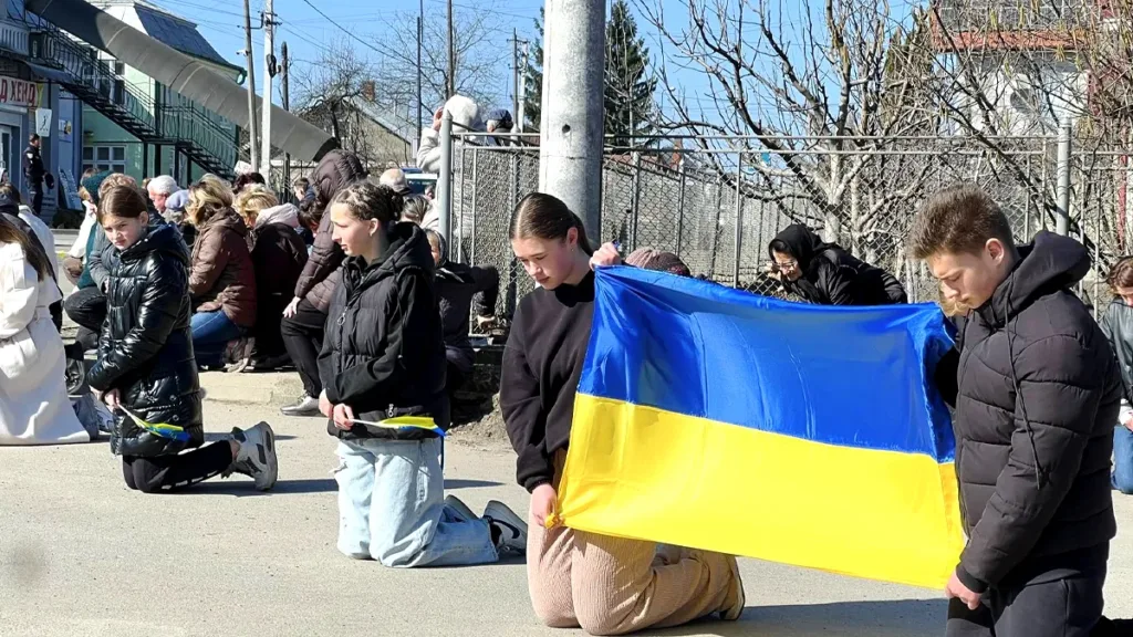 Люди на колінах з прапором України