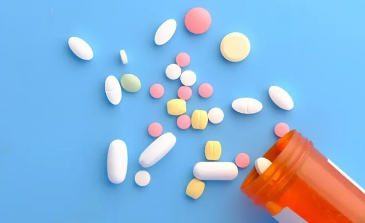 Різнокольорові таблетки поруч із пляшкою на синьому фоні